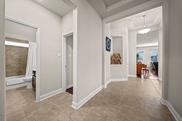 hall featuring a tray ceiling, baseboards, and tile patterned floors