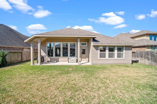 rear view of house with roof with shingles, a lawn, a patio area, and a fenced backyard