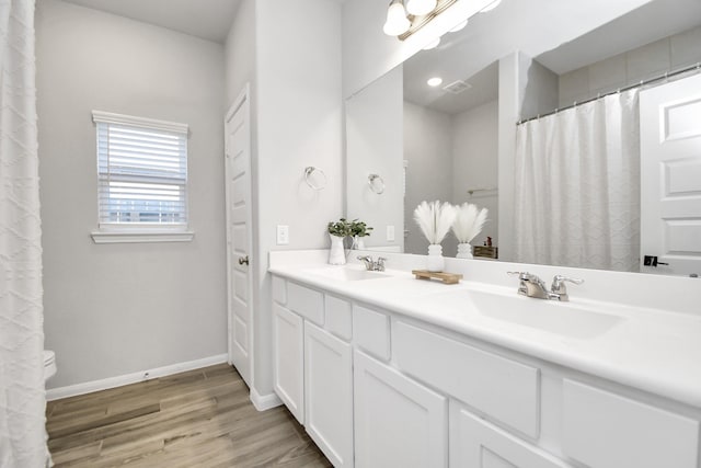 bathroom featuring double vanity, a sink, baseboards, and wood finished floors