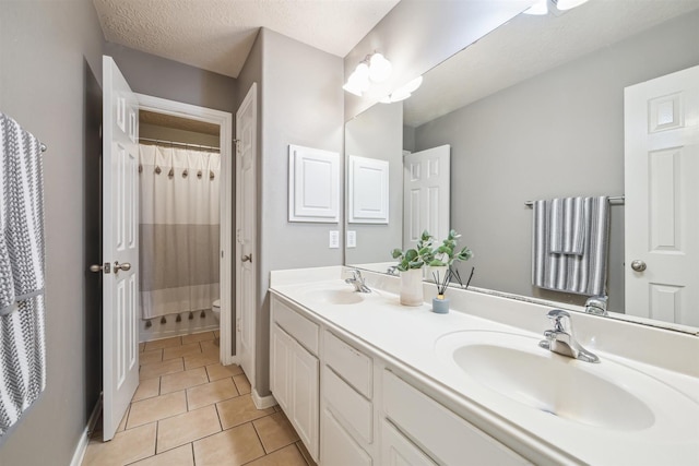 bathroom with double vanity, a textured ceiling, a sink, and tile patterned floors