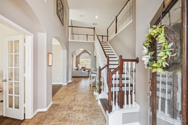 foyer with arched walkways, recessed lighting, a towering ceiling, baseboards, and stairs