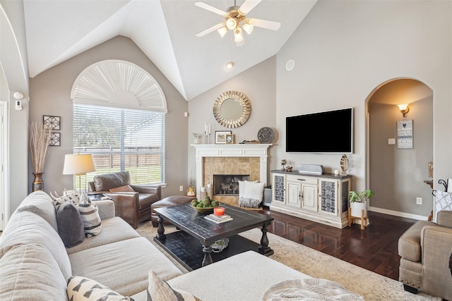 living room with arched walkways, a fireplace, dark wood-type flooring, ceiling fan, and baseboards