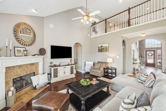 living area featuring arched walkways, a tile fireplace, a high ceiling, wood finished floors, and baseboards