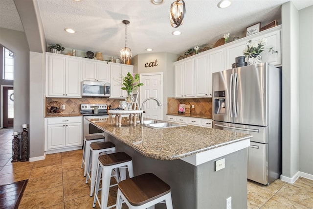 kitchen featuring a center island with sink, hanging light fixtures, appliances with stainless steel finishes, white cabinets, and a sink