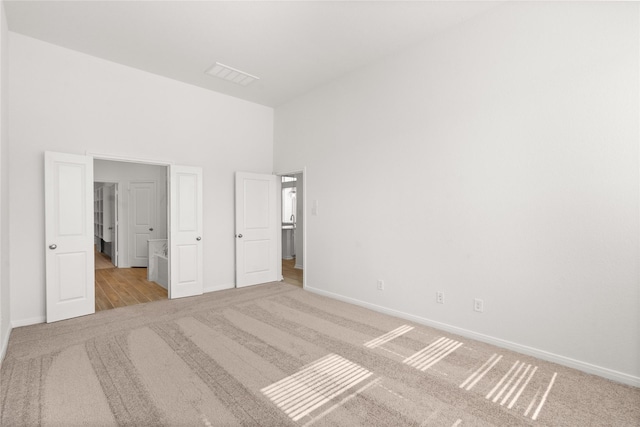 unfurnished bedroom featuring carpet, visible vents, a towering ceiling, and baseboards