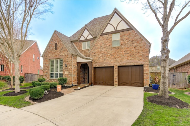 tudor house featuring brick siding, roof with shingles, fence, a garage, and driveway