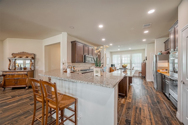 kitchen with wood finish floors, stainless steel appliances, visible vents, a peninsula, and a kitchen bar