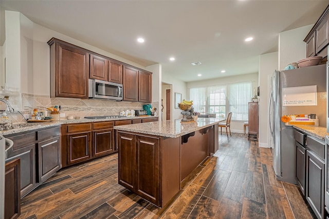 kitchen featuring appliances with stainless steel finishes, wood tiled floor, backsplash, and a center island