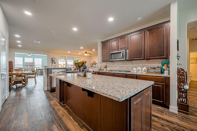 kitchen with tasteful backsplash, appliances with stainless steel finishes, dark wood-type flooring, a center island, and a peninsula