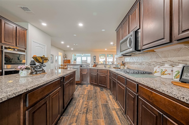 kitchen featuring light stone counters, dark wood-style flooring, stainless steel appliances, visible vents, and backsplash