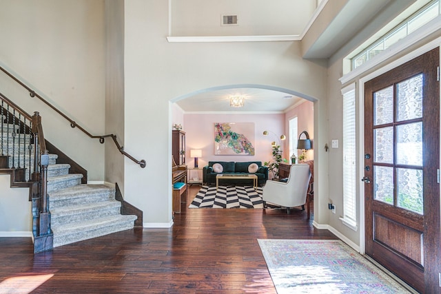 foyer with arched walkways, wood finished floors, visible vents, baseboards, and crown molding