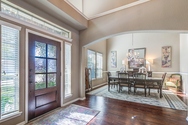 foyer entrance featuring baseboards, hardwood / wood-style floors, arched walkways, and a notable chandelier