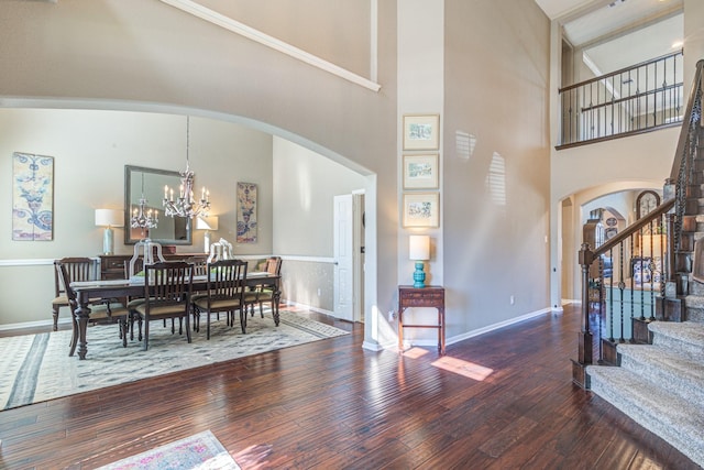 dining space with hardwood / wood-style flooring, stairway, arched walkways, and an inviting chandelier