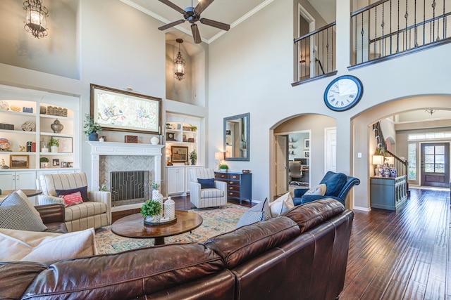 living room with arched walkways, dark wood-type flooring, a fireplace, built in features, and ornamental molding