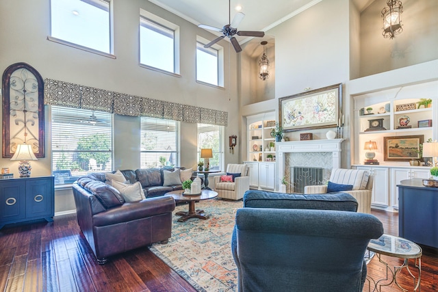 living room with built in features, a fireplace, ornamental molding, dark wood-type flooring, and ceiling fan