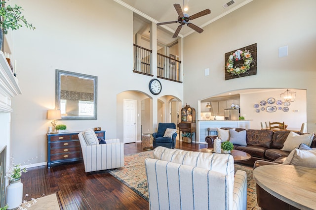 living area featuring visible vents, arched walkways, dark wood finished floors, baseboards, and ceiling fan with notable chandelier