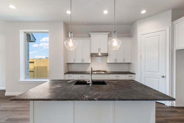 kitchen with dark wood-type flooring, under cabinet range hood, decorative backsplash, white cabinetry, and a sink