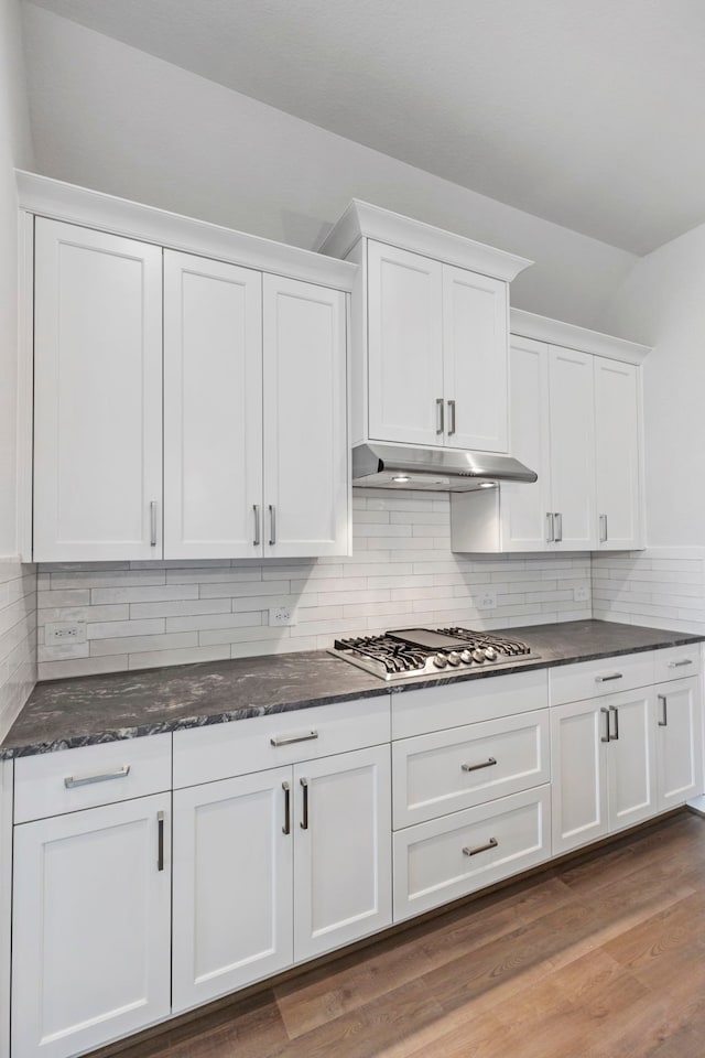 kitchen with stainless steel gas cooktop, under cabinet range hood, light wood-type flooring, dark stone countertops, and white cabinets