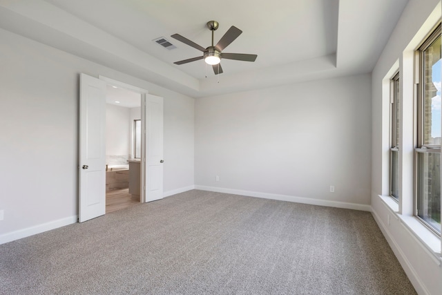 unfurnished bedroom featuring a tray ceiling, baseboards, visible vents, and carpet floors