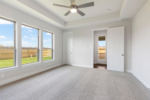 unfurnished bedroom with visible vents, a tray ceiling, carpet flooring, baseboards, and ceiling fan