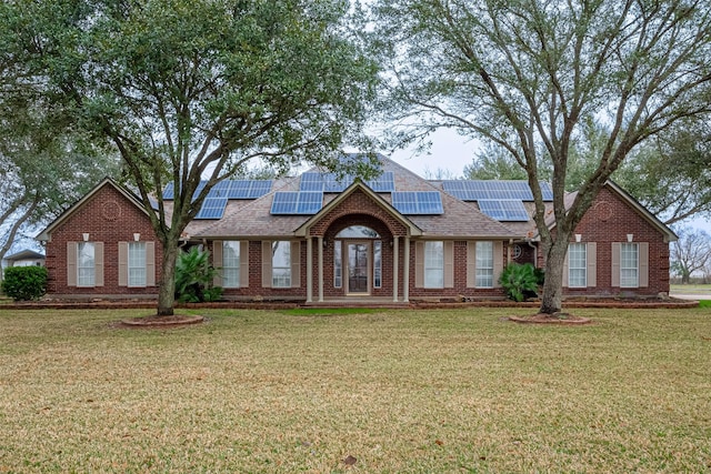 view of front of property featuring brick siding, roof with shingles, a front yard, and roof mounted solar panels