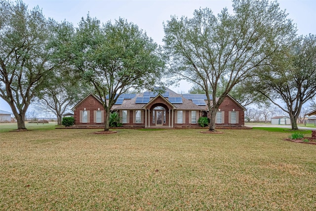 view of front of home featuring solar panels, brick siding, and a front yard