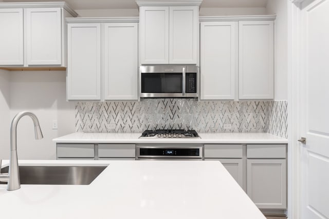 kitchen with backsplash, stainless steel appliances, light countertops, and a sink