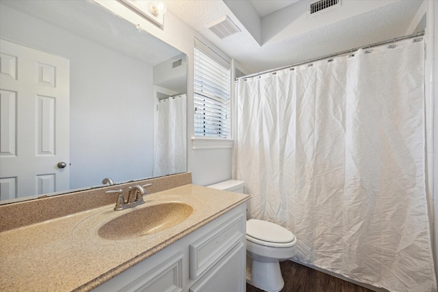 bathroom with toilet, vanity, wood finished floors, and visible vents