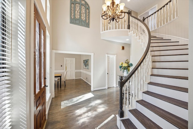 entrance foyer featuring a towering ceiling, baseboards, a chandelier, and wood finished floors