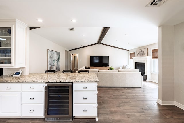 kitchen featuring beverage cooler, visible vents, lofted ceiling with beams, a peninsula, and light stone countertops