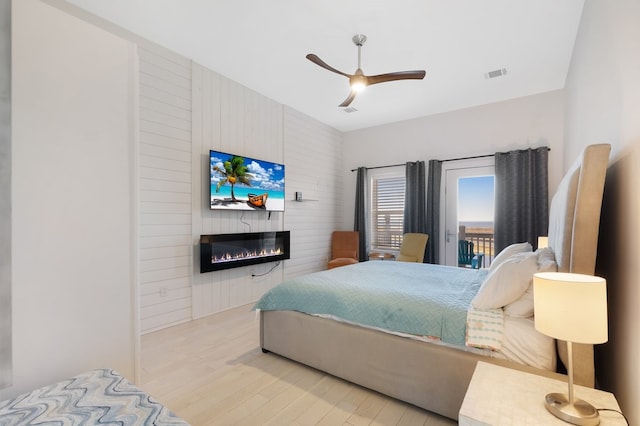 bedroom featuring visible vents, a ceiling fan, wood finished floors, access to exterior, and a fireplace