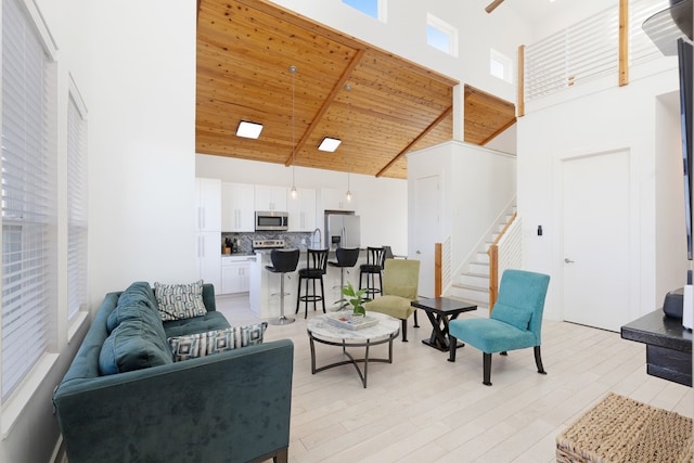 living area featuring high vaulted ceiling, light wood-type flooring, wooden ceiling, and stairs