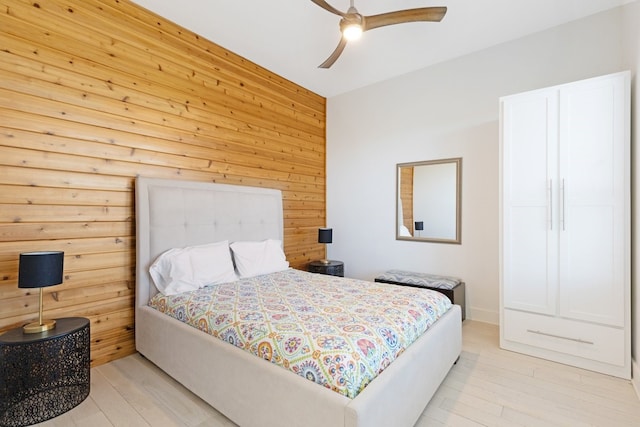 bedroom with ceiling fan, light wood-style flooring, and wooden walls