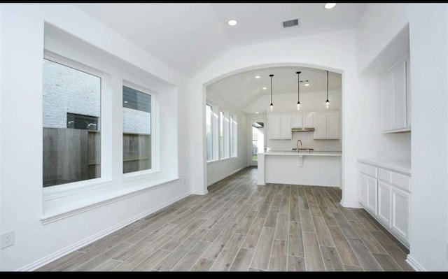 unfurnished living room with visible vents, lofted ceiling, wood finish floors, a sink, and recessed lighting