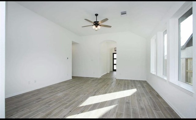 unfurnished room with wood finish floors, arched walkways, lofted ceiling, visible vents, and ceiling fan