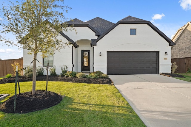 french provincial home with brick siding, concrete driveway, fence, a garage, and a front lawn