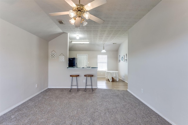 unfurnished living room featuring a textured ceiling, carpet flooring, visible vents, baseboards, and vaulted ceiling