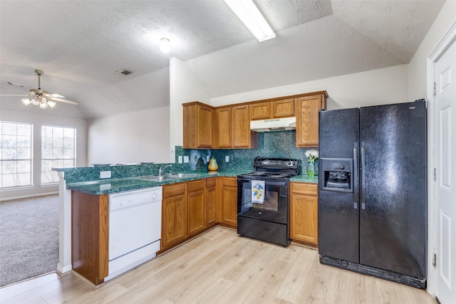 kitchen featuring lofted ceiling, under cabinet range hood, a sink, black appliances, and brown cabinetry