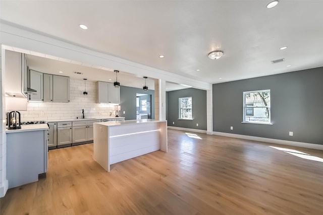 kitchen featuring light wood finished floors, light countertops, visible vents, backsplash, and baseboards