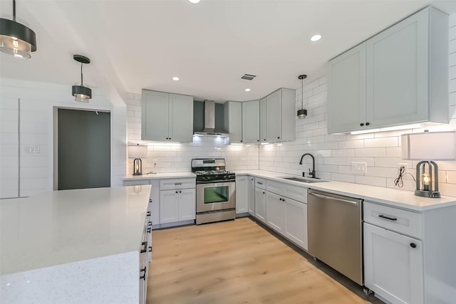 kitchen with tasteful backsplash, appliances with stainless steel finishes, light countertops, wall chimney range hood, and a sink