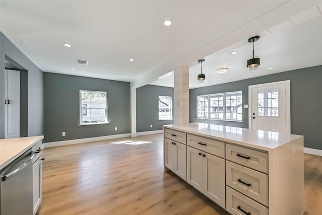 kitchen with open floor plan, stainless steel dishwasher, light wood-style flooring, and decorative columns