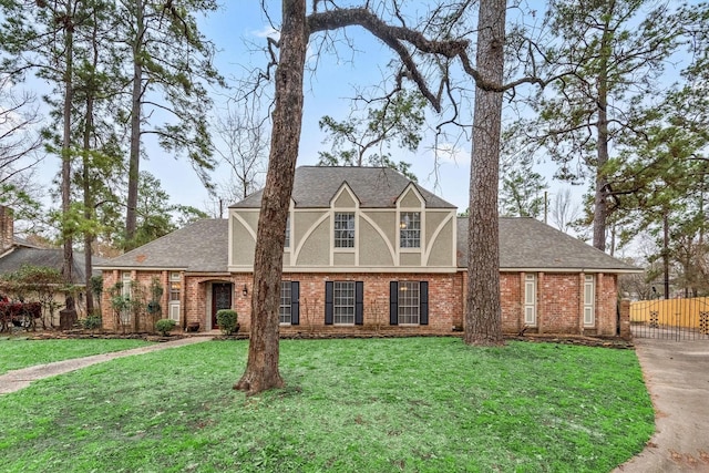 tudor home featuring a front lawn, a shingled roof, fence, and brick siding