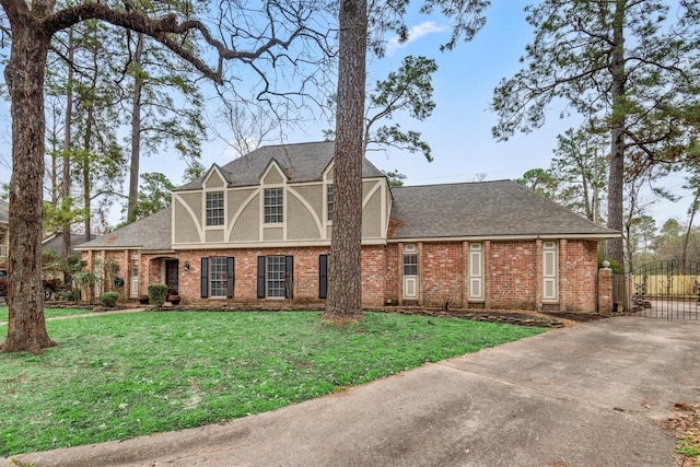 tudor house with brick siding, a shingled roof, a gate, and a front yard