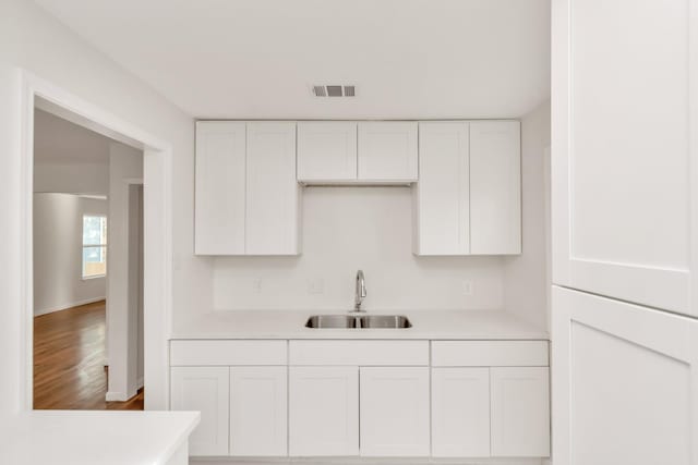 kitchen with light countertops, white cabinets, visible vents, and a sink