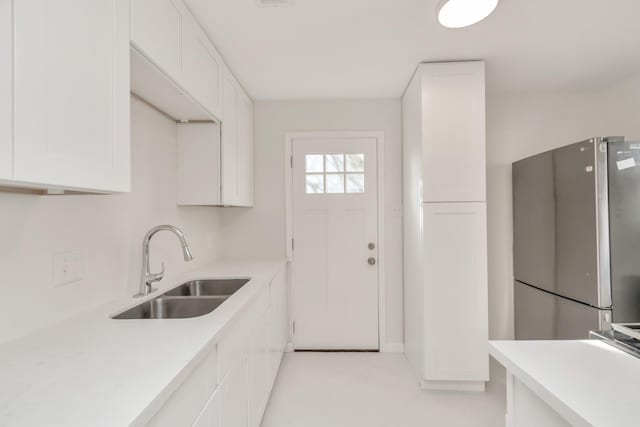 kitchen with light countertops, a sink, freestanding refrigerator, and white cabinets