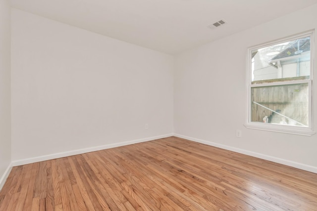 empty room featuring light wood-style floors, a wealth of natural light, visible vents, and baseboards