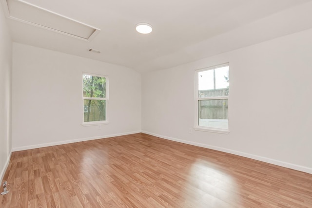 empty room featuring light wood-style floors, baseboards, visible vents, and attic access