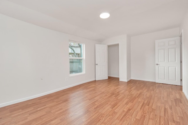 unfurnished room featuring vaulted ceiling, light wood-style flooring, and baseboards