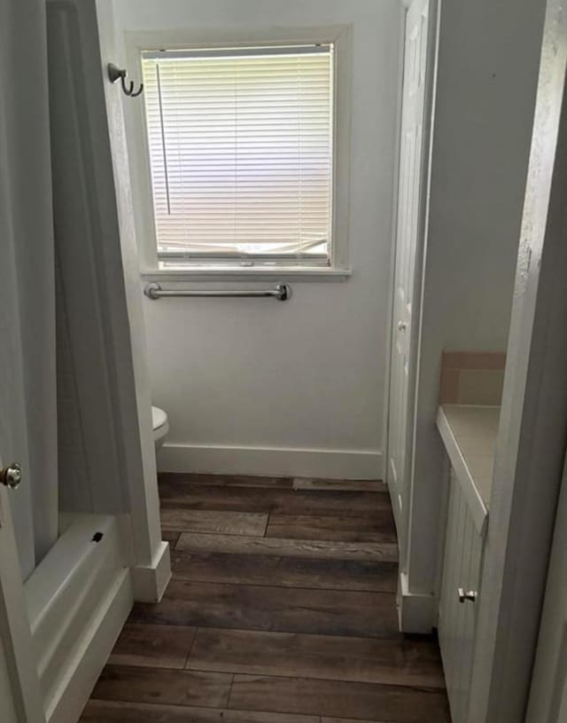 bathroom with shower / bath combination with curtain, wood finished floors, toilet, and baseboards