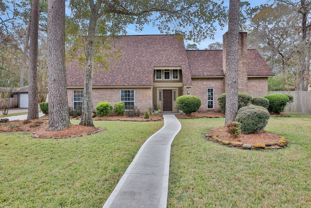 view of front facade with a shingled roof, a chimney, fence, a front lawn, and brick siding